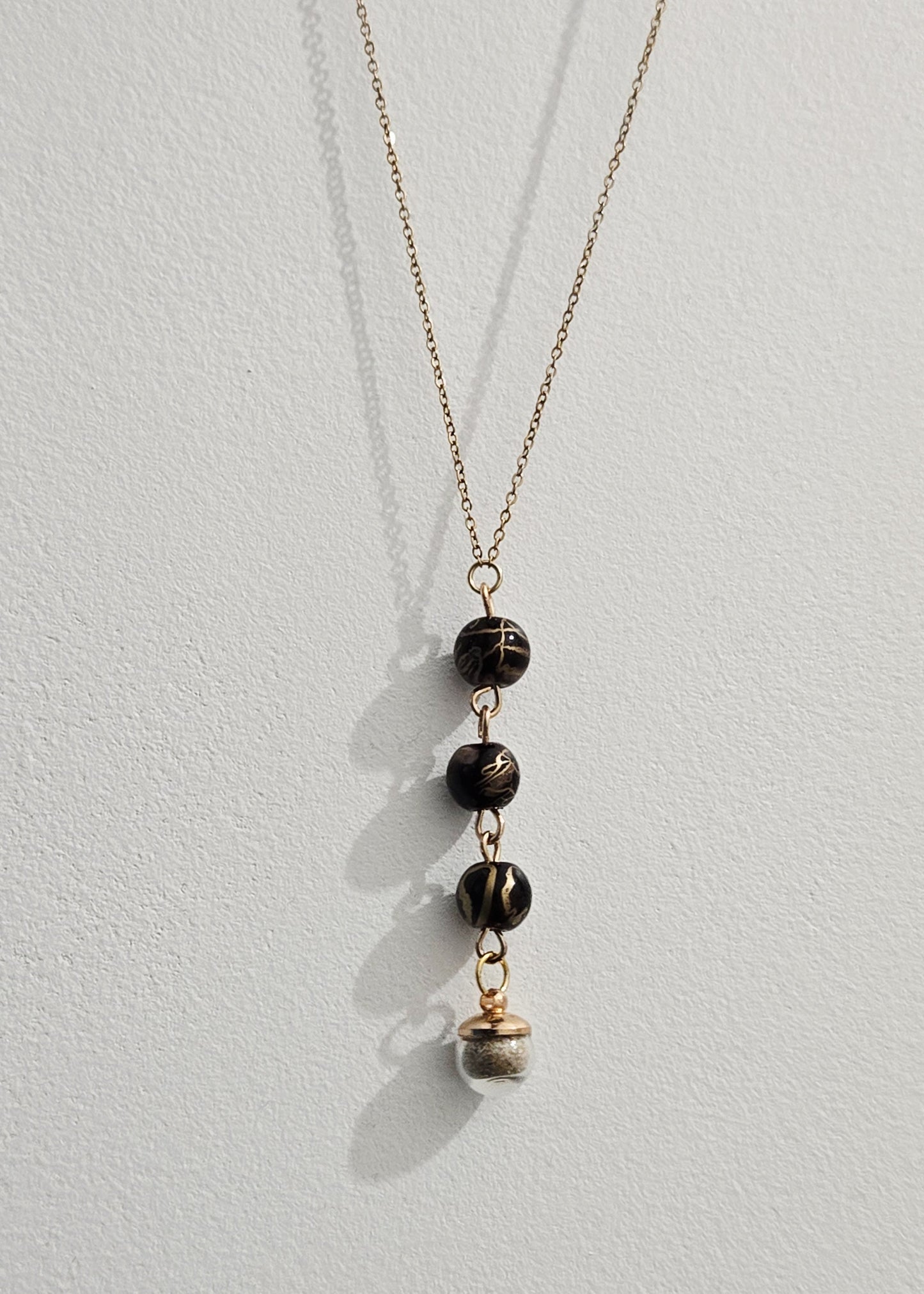 Collier noir et doré, sable de plage